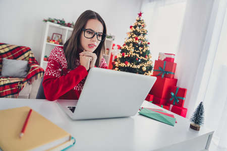 Photo of minded cute lady sit workspace look pc screen bite lip wear santa hat sweater in decorated...