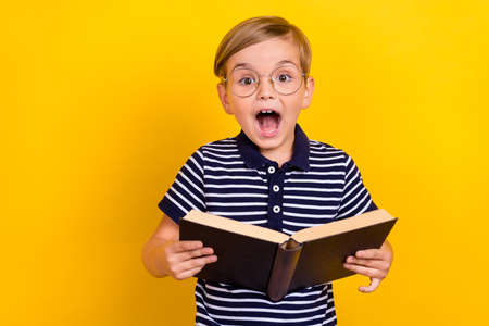 Photo portrait little boy wearing t-shirt glasses amazed reading book isolated vibrant yellow color backgroundの写真素材