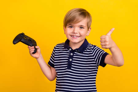 Photo portrait little boy playing video games joystick showing thumb-up isolated vibrant yellow color backgroundの写真素材