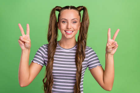 Portrait of attractive cheerful long-haired girl showing double v-sign good mood isolated over green...