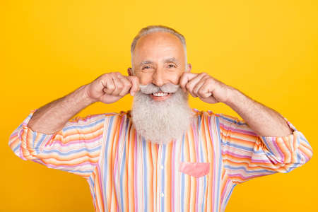 Portrait of attractive cheerful well-groomed grey-haired man touching mustache isolated over bright yellow color backgroundの写真素材