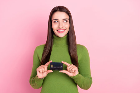 Photo of dreamy young happy cheerful woman look empty space hold credit card isolated on pink color backgroundの写真素材