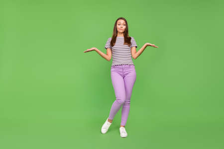 Full length photo of happy clueless young woman shrug shoulders no idea isolated on green color...