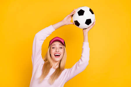 Photo portrait amazed woman in cap catching soccer ball laughing isolated bright yellow color backgroundの写真素材