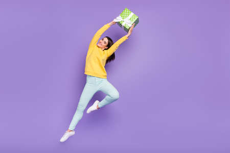 Full length body size view of attractive cheerful girl jumping holding giftbox isolated over violet...