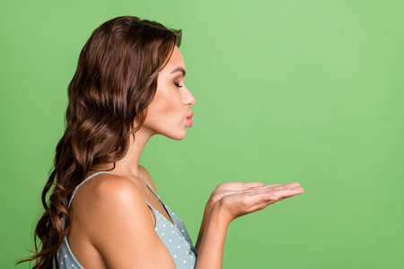 Profile side photo of dreamy pretty woman hold hand send air kiss empty space isolated on green color backgroundの写真素材