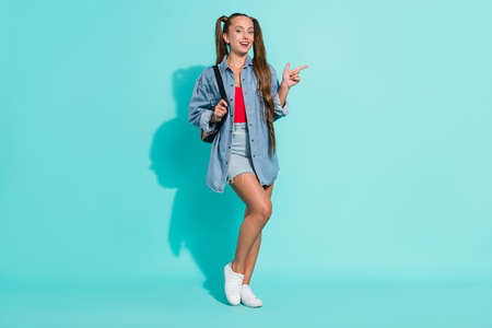 Photo of dreamy beautiful young lady wear jeans shirt rucksack smiling pointing empty space isolated...