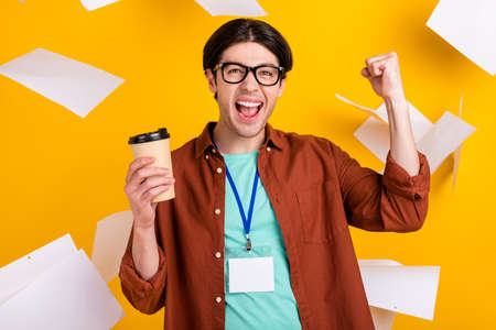 Photo of funky sweet young guy dressed brown shirt glasses smiling drinking tea rising fist isolated...