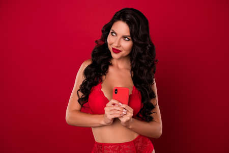 Portrait of attractive cunning sly cheery minded wavy-haired nude girl using device creating post isolated over vivid red color backgroundの写真素材