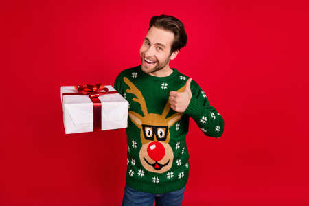 Photo of good mood positive smiling handsome man hold present show thumb-up isolated on red color backgroundの写真素材