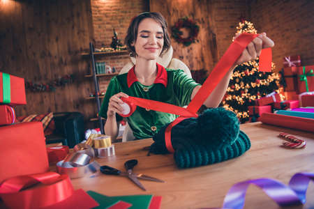 Photo of sweet cute young lady wear elf clothes packaging new year present smiling indoors house...