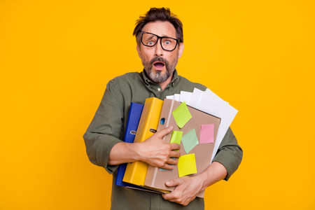 Photo portrait businessman keeping documents amazed worked in night shift isolated vivid yellow color backgroundの写真素材