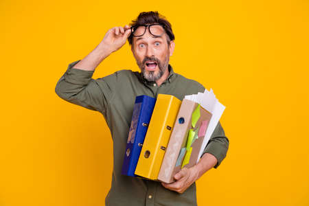Photo portrait man wearing shirt amazed in glasses keeping papers in office isolated vivid yellow color backgroundの写真素材