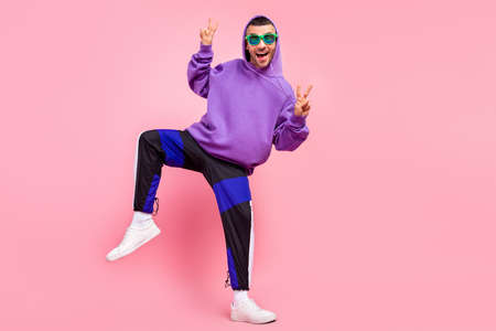 Full length photo of cool young brunet guy dance show v-sign wear eyewear hoodie pants shoes isolated on pink backgroundの写真素材