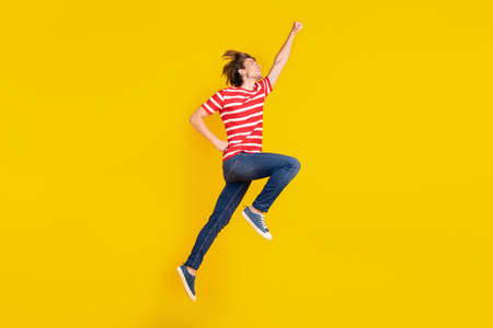 Photo of cute strong young man wear striped t-shirt jumping high looking empty space isolated yellow color backgroundの写真素材