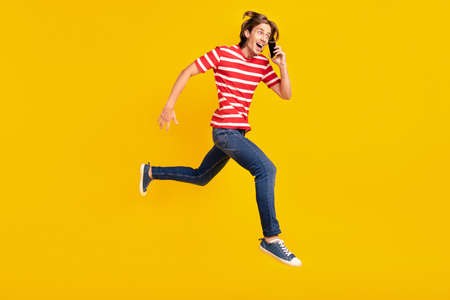 Photo of impressed cute man wear striped t-shirt running talking modern device looking empty space isolated yellow color backgroundの写真素材