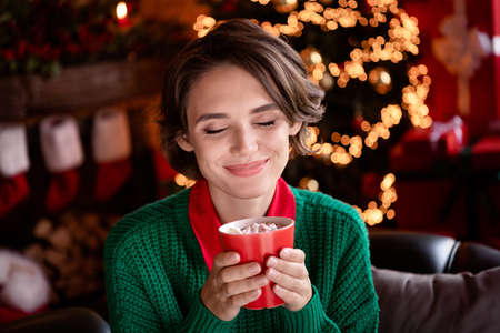 Photo of cute pretty young lady wear green pullover smiling enjoying tasty beverage indoors house home roomの写真素材