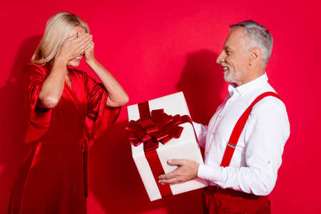 Profile side photo of senior husband give gift his wife close eyes advent spirit anniversary lovers isolated over red color backgroundの写真素材