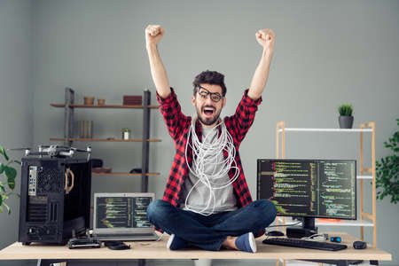 Portrait of attractive cheerful amazed lucky funky guy sitting on table celebrating dev solution indoor at work place stationの写真素材