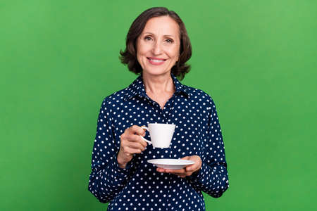 Photo of cute old lady drink tea wear dotted blouse isolated on green color background