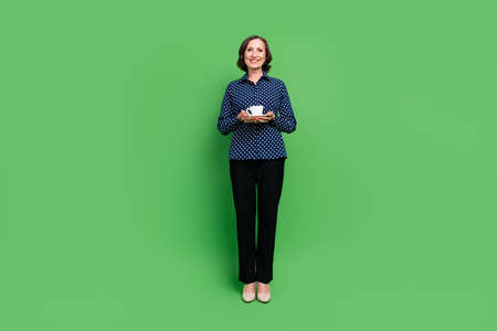 Full size photo of aged lady hold cup wear shirt pants high heels isolated on green color backgroundの写真素材