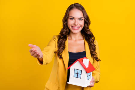 Photo of shiny beautiful young lady wear suit jacket inviting you holding arms hands small house smiling isolated yellow color backgroundの写真素材