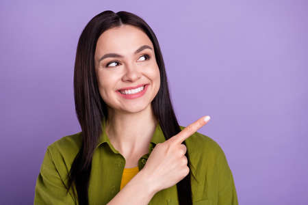 Photo of dreamy shiny young lady dressed green clothes smiling looking pointing finger empty space isolated purple color backgroundの写真素材