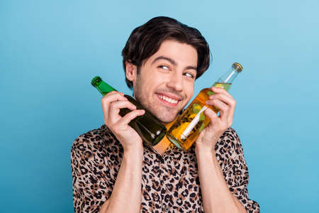Portrait of attractive cheerful guy drinking holding bottles beer enjoying isolated over bright blue color backgroundの写真素材