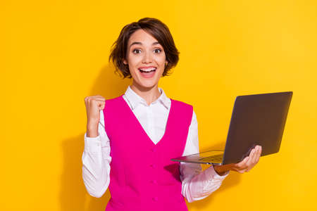 Photo of pretty lucky young woman dressed pink suit smiling chatting modern gadget rising fist isolated yellow color backgroundの写真素材