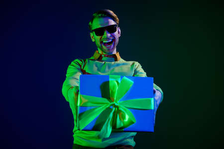 Photo of attractive young positive man hold hand surprise gift box give you holiday isolated on neon backgroundの写真素材