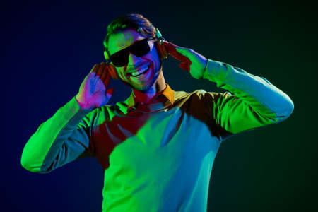 Photo of young cool guy listen music wear spectacles headphones sweater isolated on dark color...