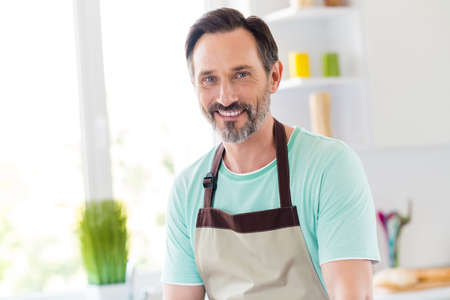 Photo of handsome bearded mature man shiny smile beaming smile wear apron blue t-shirt home kitchen indoorsの写真素材