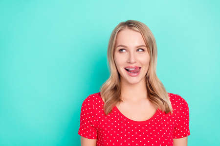 Photo portrait blonde woman licking lips looking blank space dotted red t-shirt isolated vibrant turquoise backgroundの写真素材