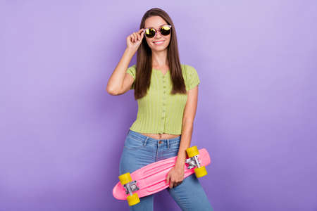 Portrait of attractive cheerful content girl touching specs holding skate isolated over purple violet color backgroundの写真素材