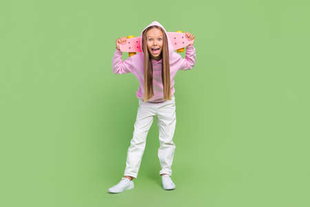 Full size photo of impressed small blond girl hold skate wear hoodie trousers sneakers isolated on green backgroundの写真素材