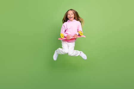 Full size photo of cute small blond girl jump with skate wear hoodie trousers sneakers isolated on...