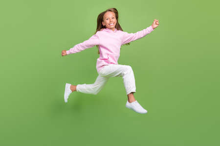 Full body photo of cool little blond girl run wear sweatshirt trousers sneakers isolated on green backgroundの写真素材