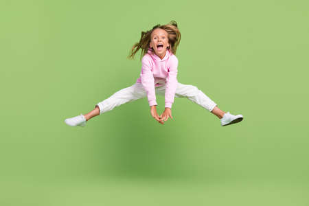 Full length photo of funky small blond girl jump wear sweatshirt trousers sneakers isolated on green backgroundの写真素材