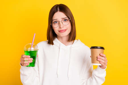 Photo of funny doubtful young lady wear white hoodie holding coffee cocktail isolated yellow color...
