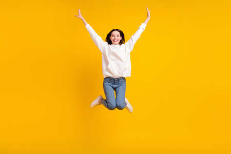 Photo of funky cheerful lady jump raise hands wear white hoodie jeans footwear isolated yellow color backgroundの写真素材