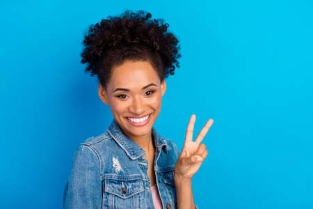 Photo of cheerful positive happy afro american woman show v-sign good mood isolated on blue color...