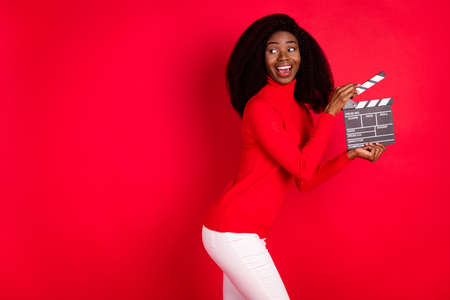 Profile portrait of funny dark skin girl hold clapboard look empty space open mouth smile isolated...