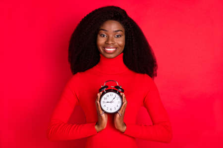 Photo of young black woman happy positive smile hold timer clock alarm isolated over red color...