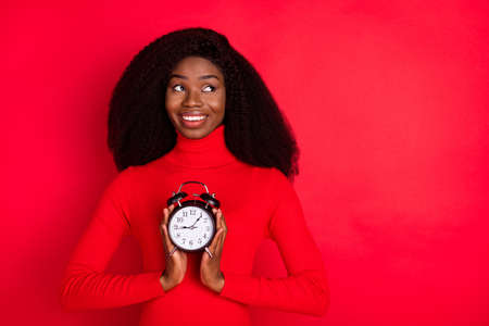 Photo of young black woman happy positive smile hold timer clock alarm look empty space isolated over red color backgroundの写真素材