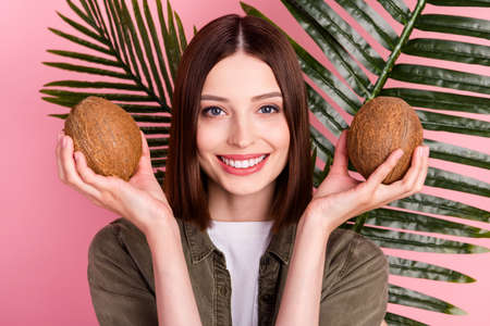 Photo of funny brunette hairdo young lady hold coconuts wear green shirt isolated on pink color backgroundの写真素材