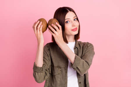 Photo of think brunette hairdo millennial lady hear coconuts wear khaki shirt isolated on pink color...