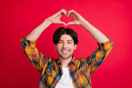 Photo of flirty adorable young gentleman wear plaid outfit smiling showing fingers heart isolated red color backgroundの写真素材