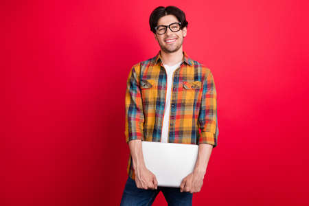 Photo of charming pretty young gentleman wear plaid outfit spectacles smiling holding modern device isolated red color backgroundの写真素材
