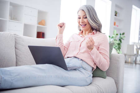 Photo of hooray wavy hairdo aged lady look laptop wear pink shirt jeans sit at home aloneの写真素材