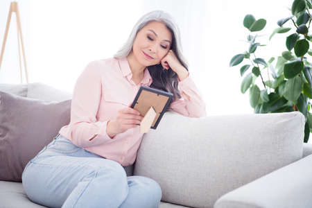 Photo of thinking long hairdo aged lady look photo wear pink shirt jeans sit at home alone